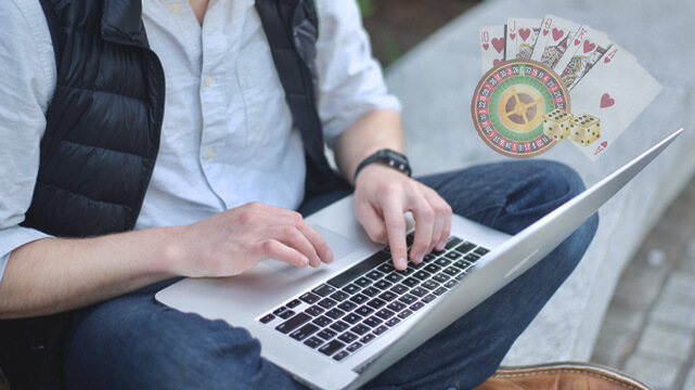 Guy Sitting Down Using Laptop, Roulette Wheel, Poker Cards, Dice