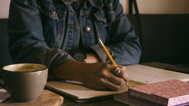 Woman Sitting Writing in Notebook, Coffee on Table