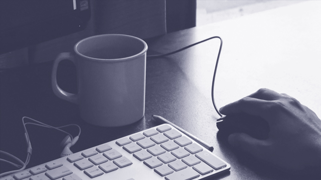 Closeup of Hand on a Computer Mouse Next to Keyboard and Coffee